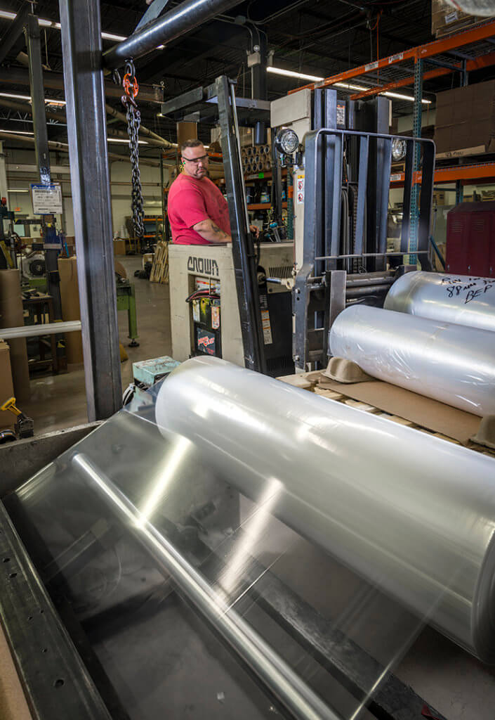 Tagline employee operates forklift to lift a roll of thin LDPE film